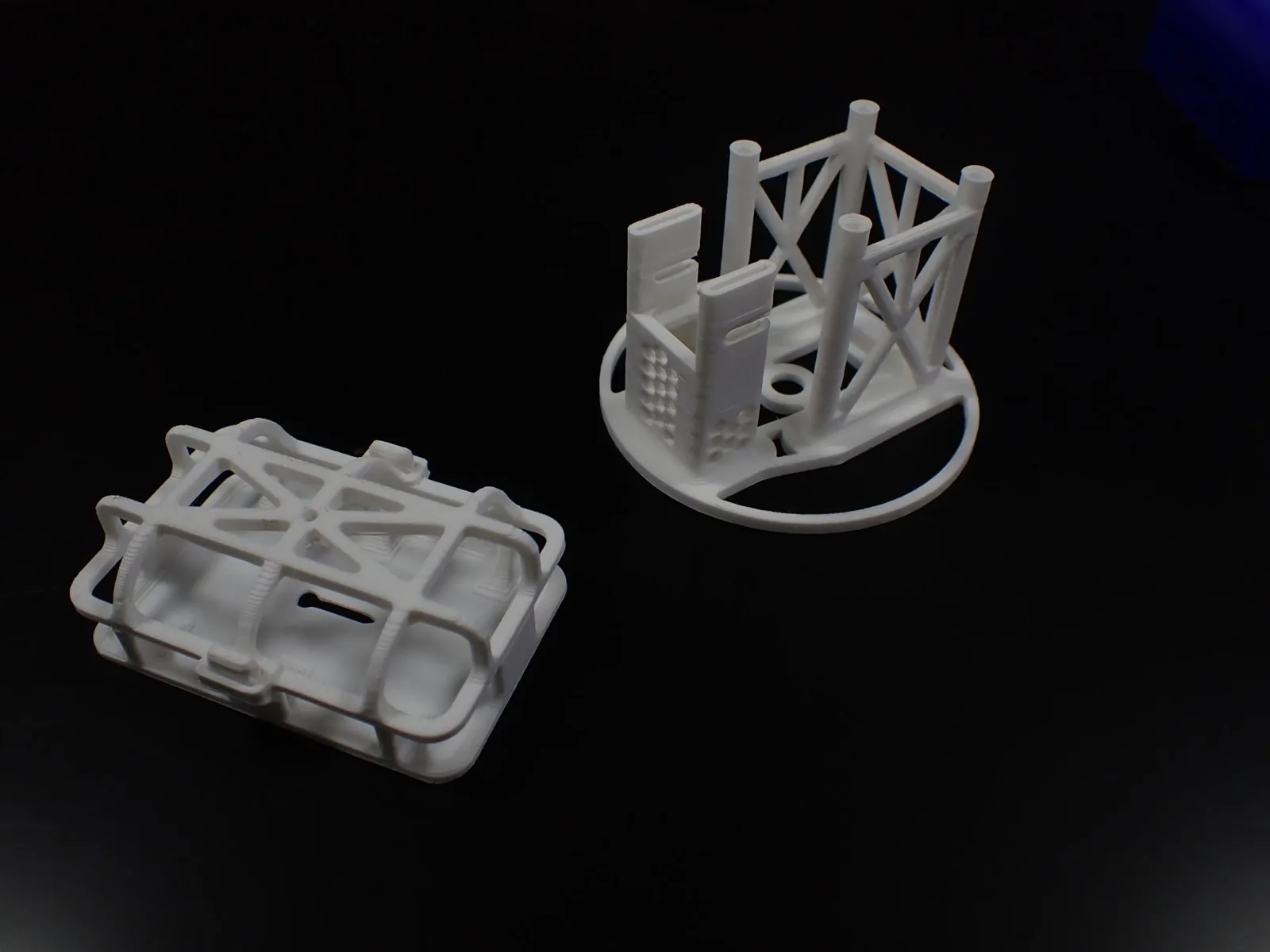 3D printed topology-optimised payload holder and battery cradle, white lattice-structure parts on a dark surface.