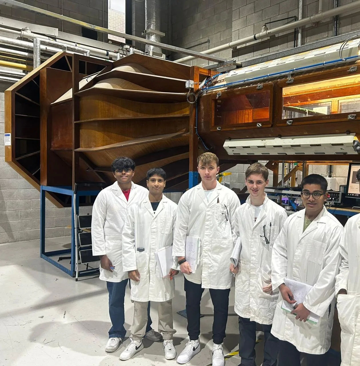 The project group of five in white lab coats in front of the wind tunnel.